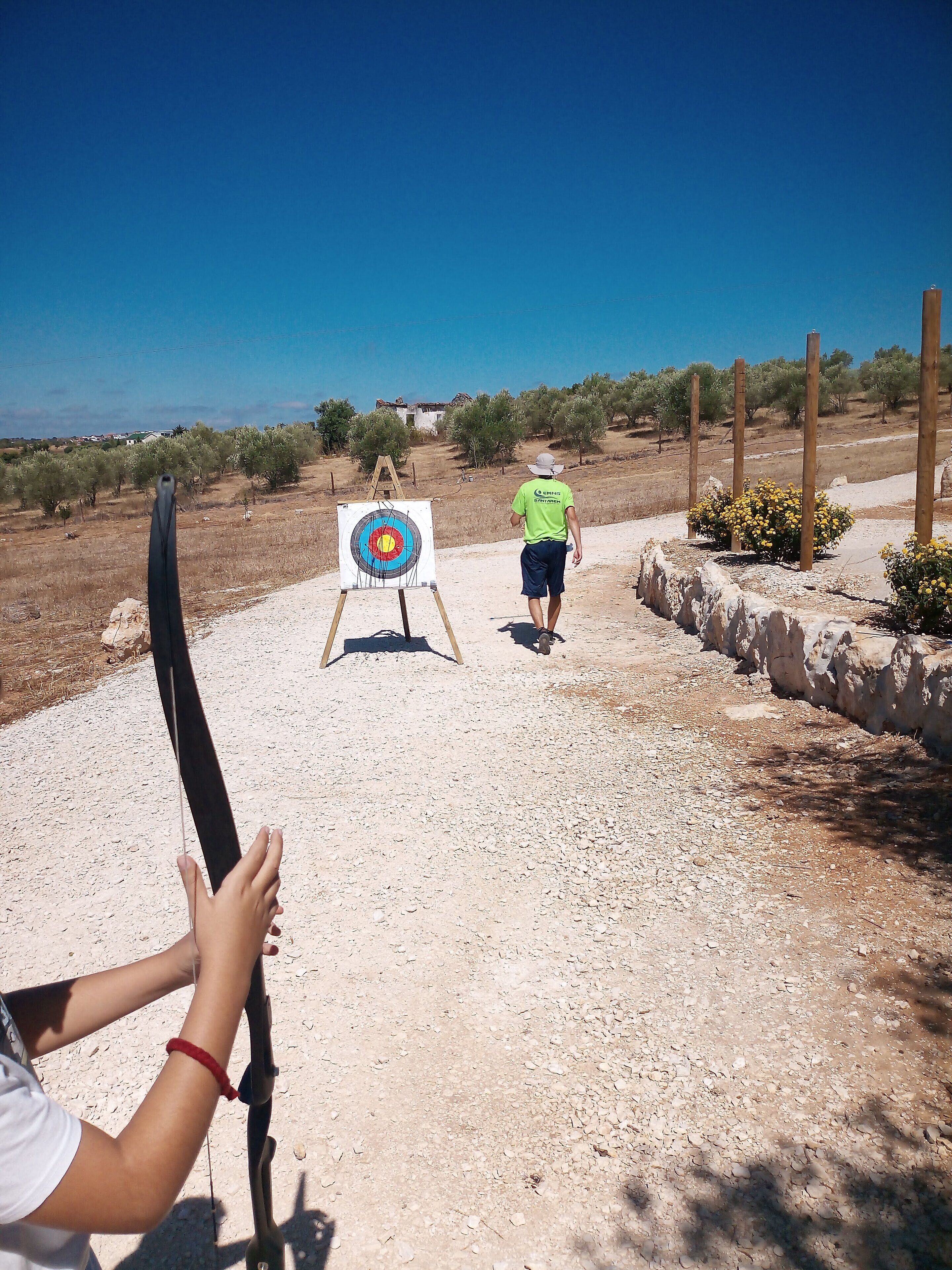 An outdoor archery range with a target in the distance, surrounded by a dry landscape and sparse vegetation.