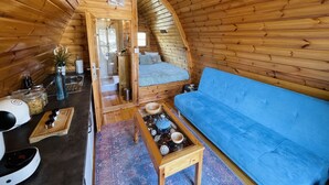Interior acogedor de una cabaña con detalles de madera, un sofá azul, una mesita y una zona de kitchenette.