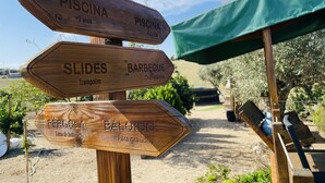 Un letrero de madera con varios indicadores de dirección que señalan servicios como piscina, toboganes, zona de barbacoa y jardín.