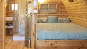 Un acogedor interior de cabaña de madera con baño, una cama y un lavabo de madera decorado con guijarros.