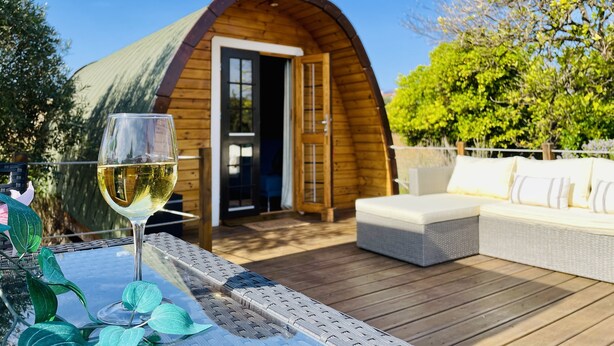 Una cabaña de madera con techo curvo, puerta de vidrio y una terraza con mobiliario exterior.