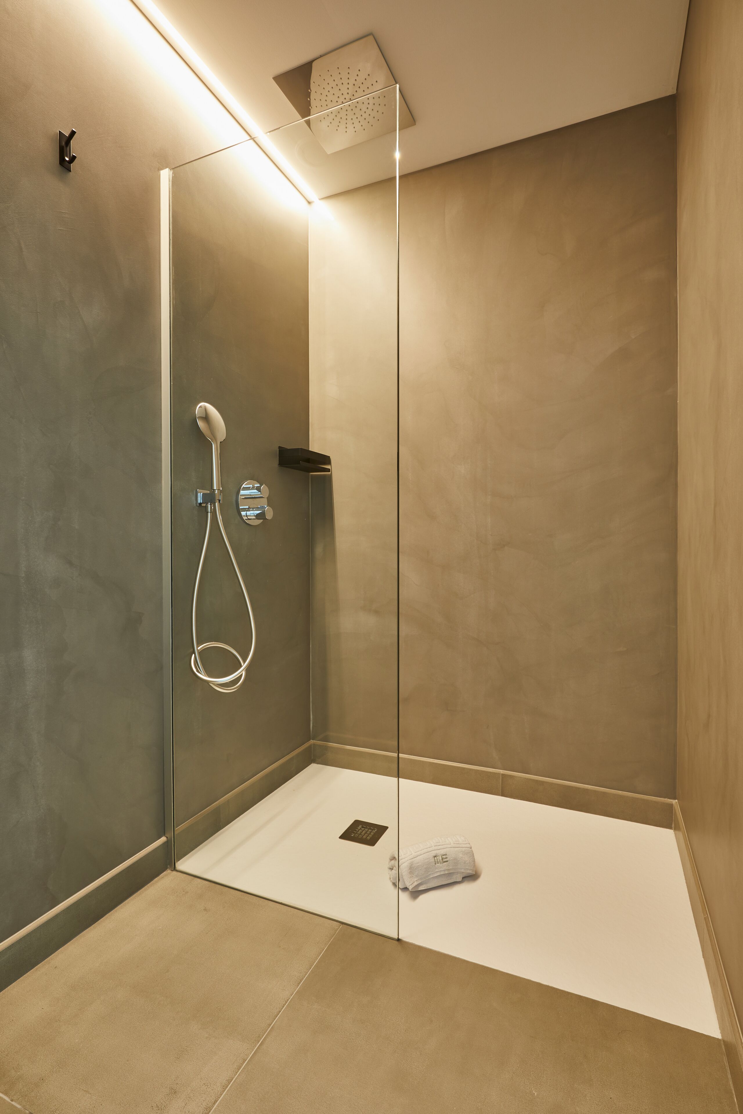 A modern shower area with a glass door, a handheld showerhead, and a towel on the floor.