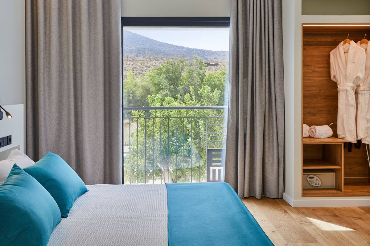 Een slaapkamer met een bed, een kledingkast en een balkon met uitzicht op bomen en heuvels.