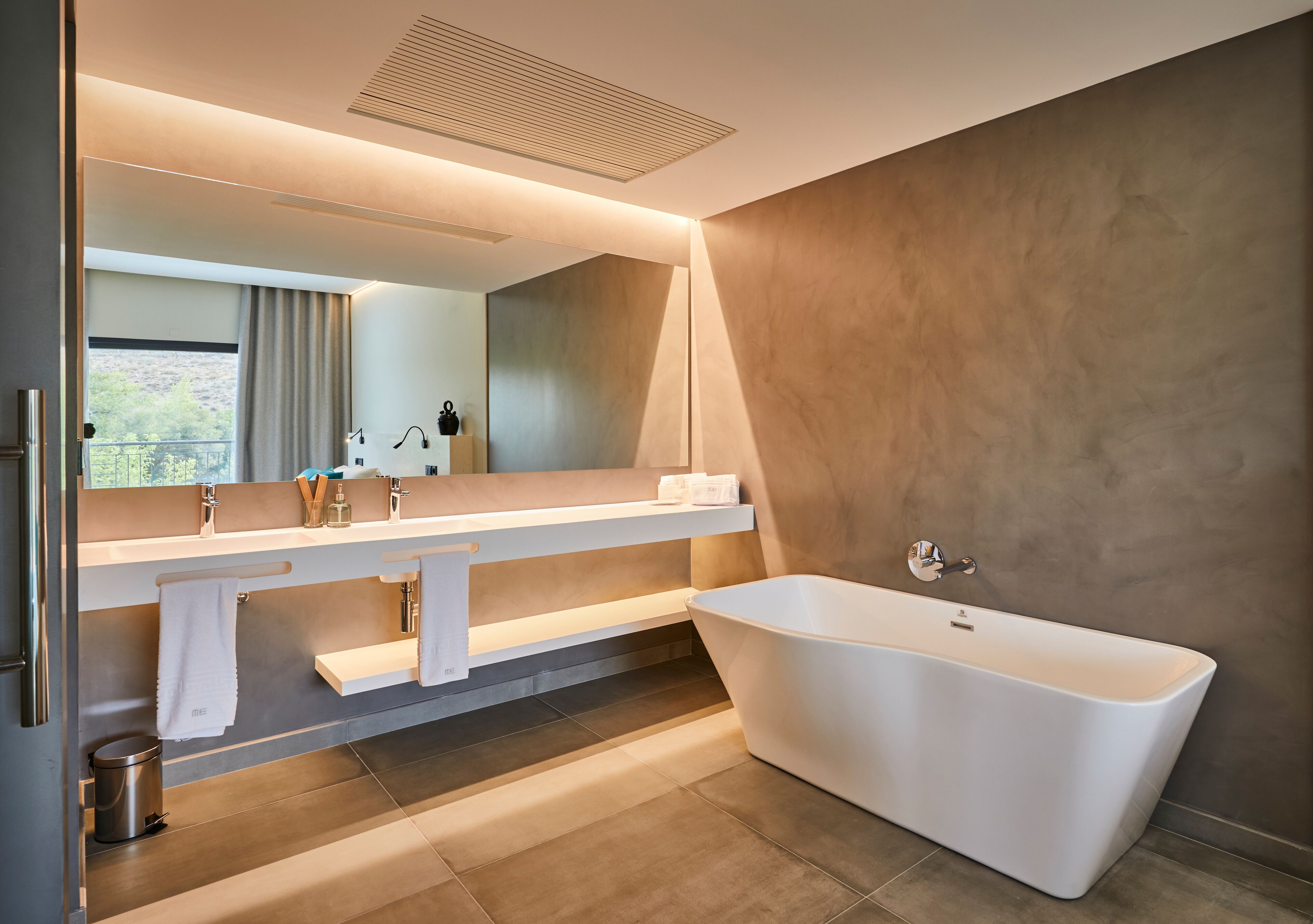 A modern bathroom with a freestanding bathtub, a large mirror, and a vanity with multiple sinks and towel racks.