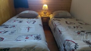 Two single beds with patterned bedding, a nightstand with a heart-shaped lamp, and wooden walls.