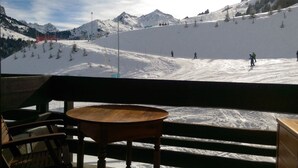 A ski slope with skiers and a chairlift, viewed from a wooden bench with a table.