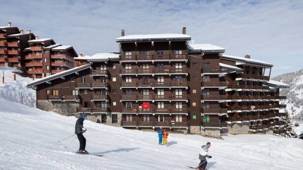 A multi-story hotel with balconies, ski slopes, and a ski lift in the background.
