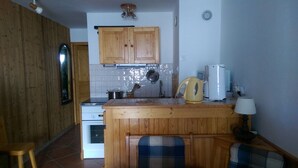 A compact kitchen with wooden cabinets, a white stove, and a small island with a kettle and coffee maker.