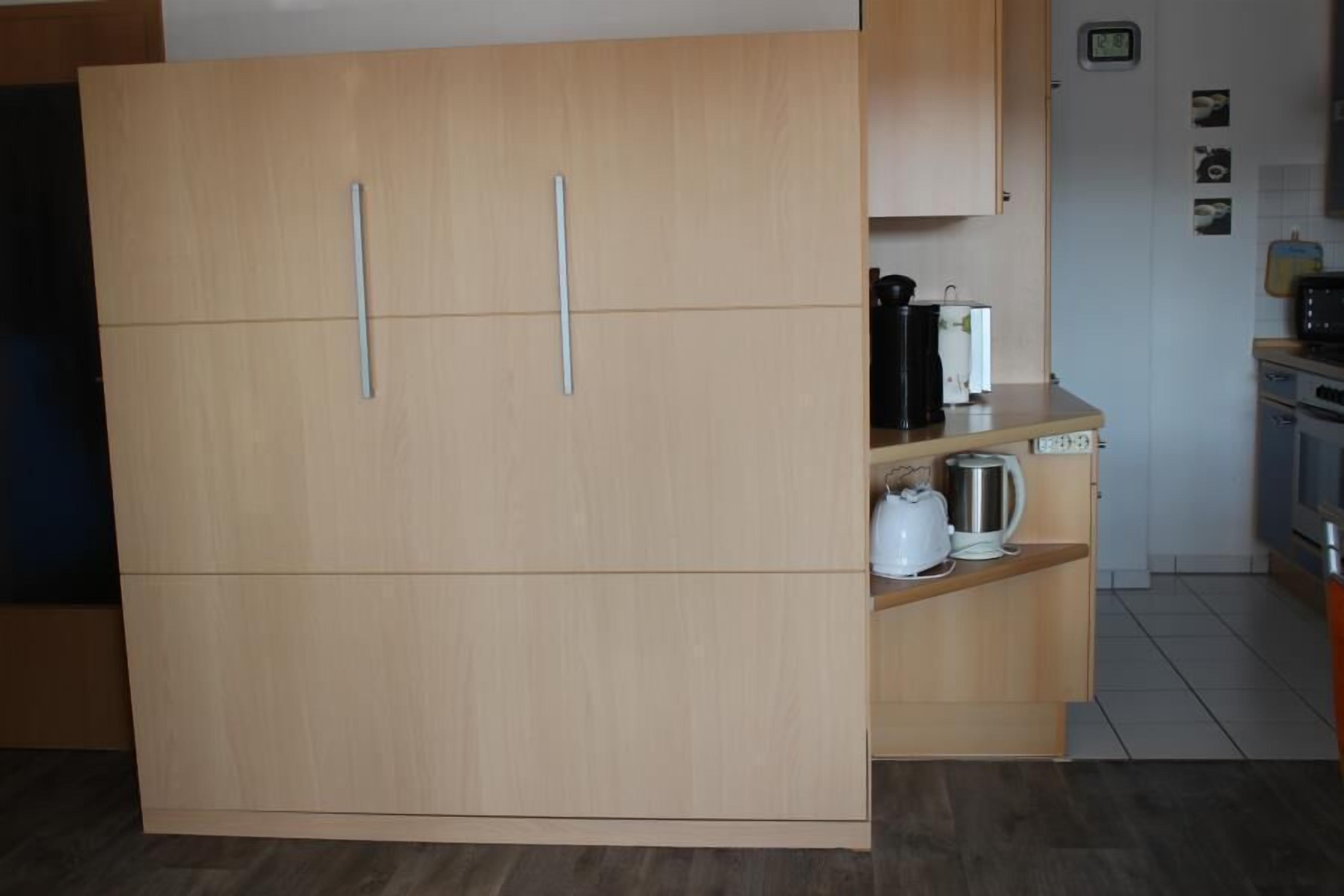 A kitchen with a wooden cabinet, a microwave, a kettle, and a toaster.