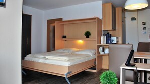 A compact room with a bed, a desk, a chair, a small table, a lamp, and a potted plant. - Haus Seewind 10 (Cuxhaven)