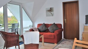 A room with a red sofa, two wicker chairs, a wooden table, and a door. - Haus Heidehof (Cuxhaven)