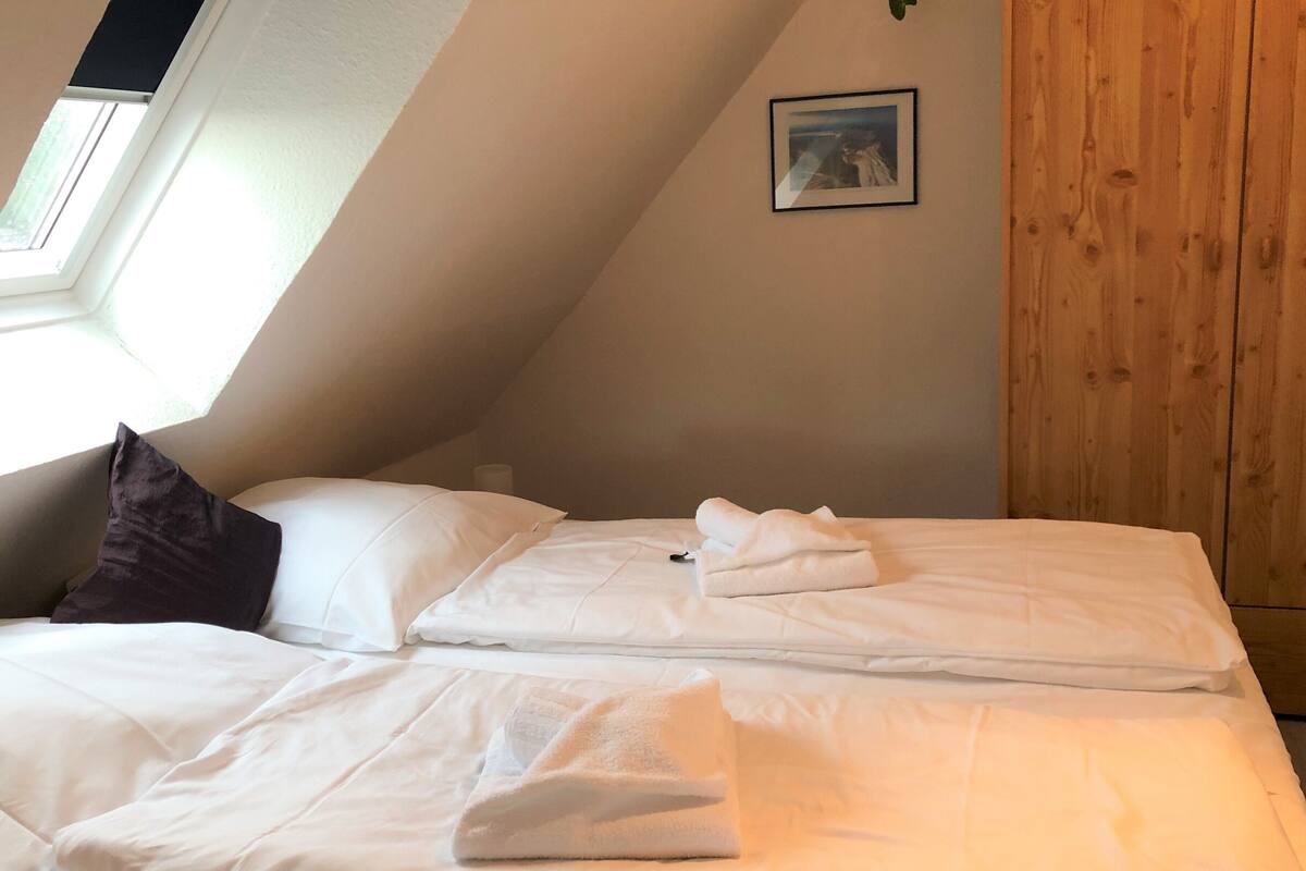 Une chambre avec un plafond en pente, une fenêtre, un mur en bois et un tableau encadré accroché au mur.