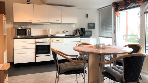 A modern kitchen with white cabinets, a microwave, an oven, and a dining area with a round table and chairs. - Haus Heidehof (Cuxhaven)