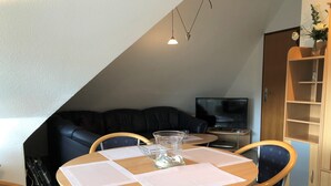 A cozy living room with a round wooden table, two blue chairs, a glass vase, and a black leather sofa. - Haus Heidehof (Cuxhaven)