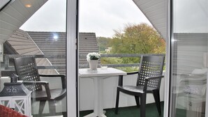 A balcony with two chairs and a small table, a white railing, and a view of trees and buildings. - Haus Heidehof (Cuxhaven)