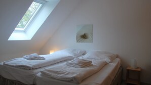 A bedroom with a skylight, a bed with white linens, a bedside table with a lamp, and a wall art piece. - Haus Heidehof (Cuxhaven)