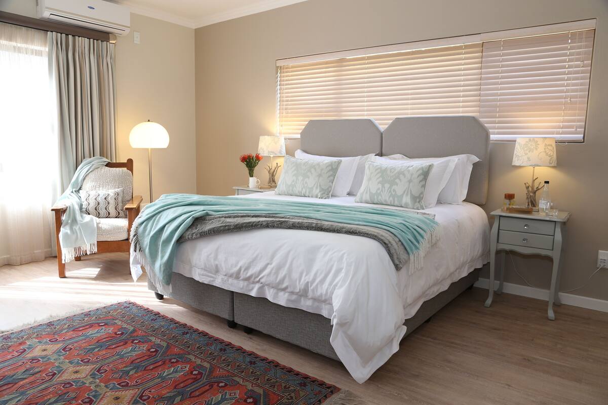 Quarto com cama, mesas de cabeceira, uma cadeira, tapete e janela com persianas.