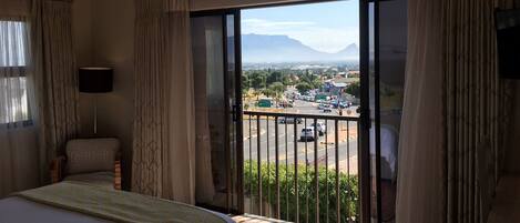 A hotel room with a bed, a chair, a balcony with a view of a cityscape and mountains.