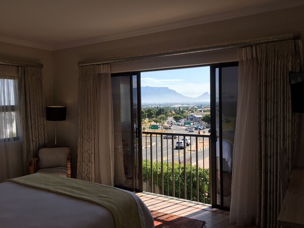 A hotel room with a bed, a chair, a balcony with a view of a cityscape and mountains.