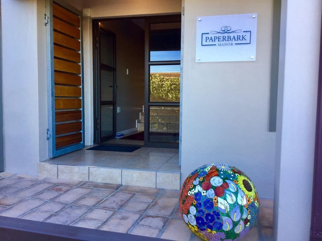 L’entrée de la propriété, appelée PAPERBARK MANOR, se distingue par un design moderne, avec une porte en verre et une sculpture en mosaïque aux couleurs vives.