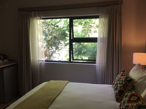A hotel room with a bed, a bedside table, a lamp, and a window with curtains.