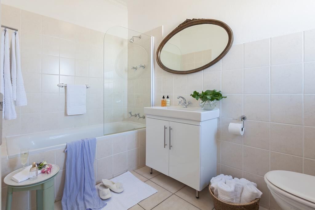 Un baño con bañera, lavabo con espejo, inodoro y una mesita con artículos de aseo.