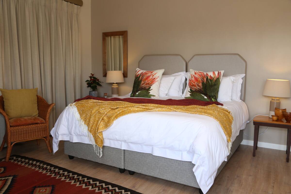 Quarto bem organizado com uma cama, uma cadeira, uma mesa de cabeceira e um abajur.