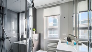 Une salle de bain moderne avec une douche à l’italienne en verre, des toilettes blanches et un grand miroir au-dessus du lavabo.