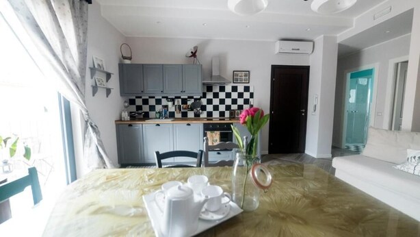 Un coin repas avec une table mise pour le thé, un vase rempli de fleurs et, au fond, une cuisine.