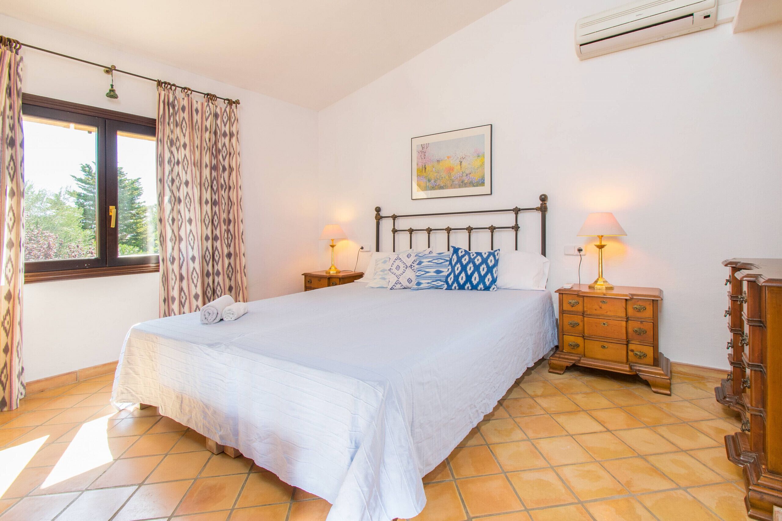 Quarto com uma cama grande, duas mesas de cabeceira com abajures, um penteadeira e uma janela com cortinas.