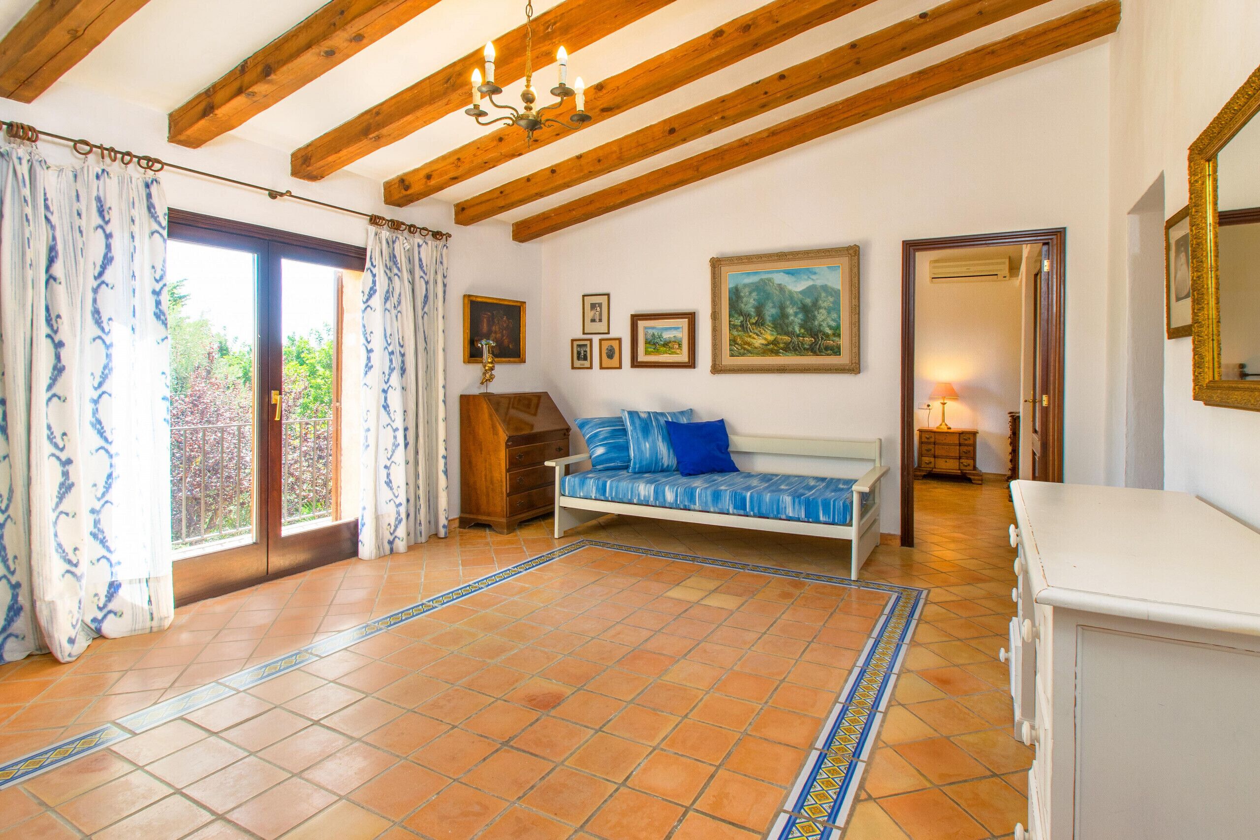 Una habitación con techo de madera, un sofá con cojines azules, un armario de madera y piso de baldosas.