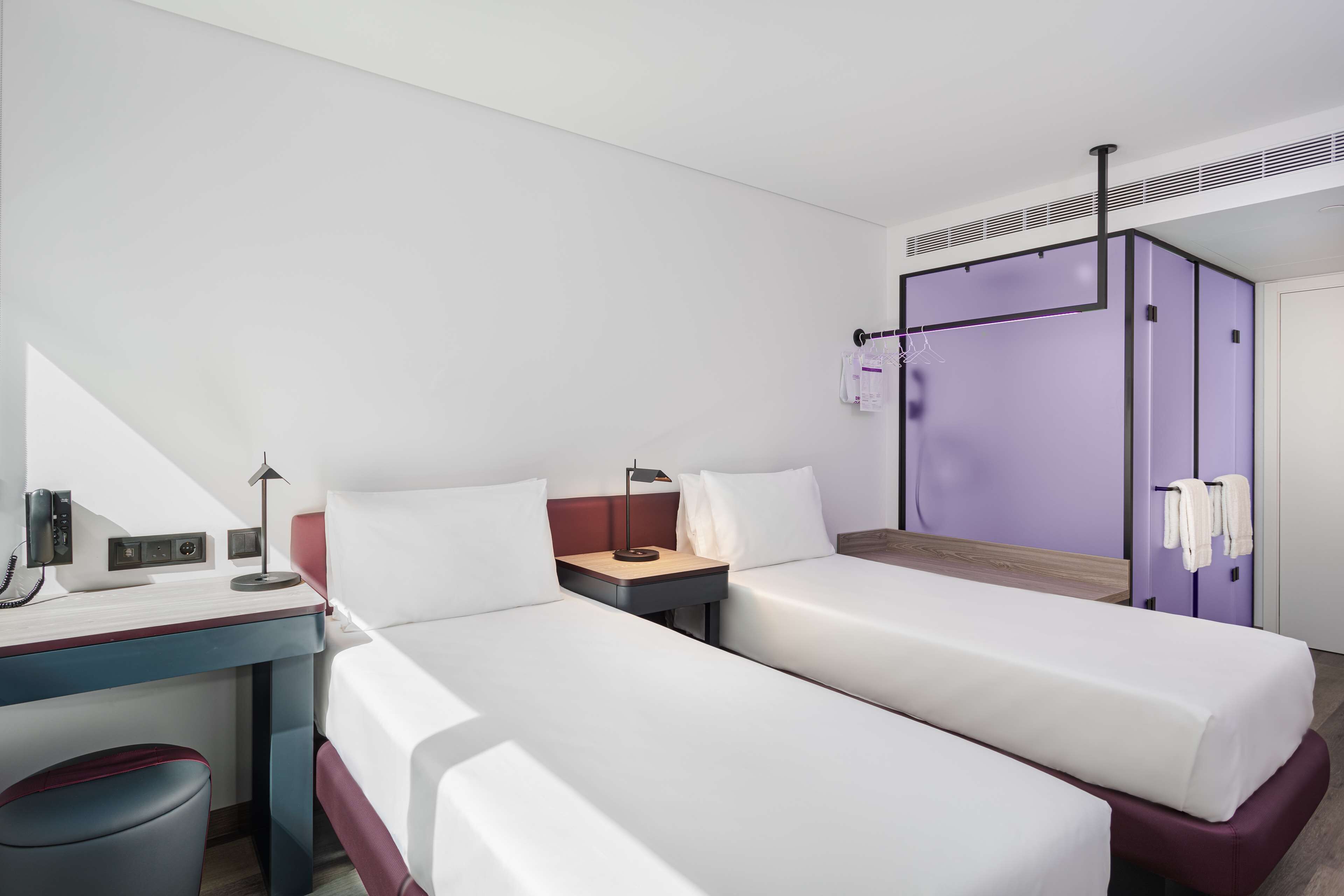A hotel room with two single beds, a desk with a telephone, and a wardrobe.