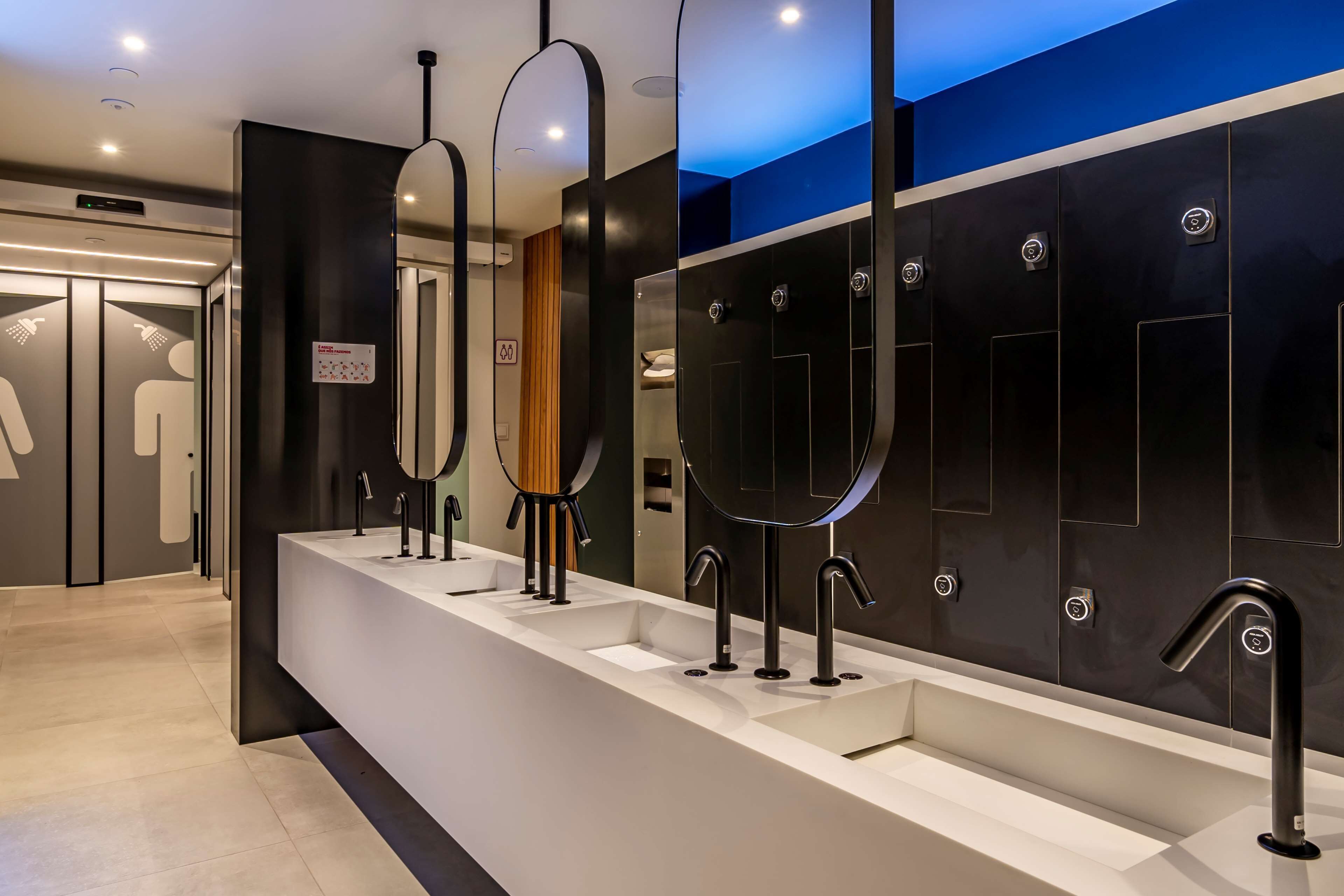 Une salle de bain moderne avec trois lavabos, chacun étant équipé d’un miroir et d’un robinet. Une pancarte indique qu’il s’agit d’une salle de bain familiale.