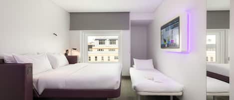 Una habitación de hotel moderna con una cama grande, una cama más pequeña, un escritorio y un espejo amplio.