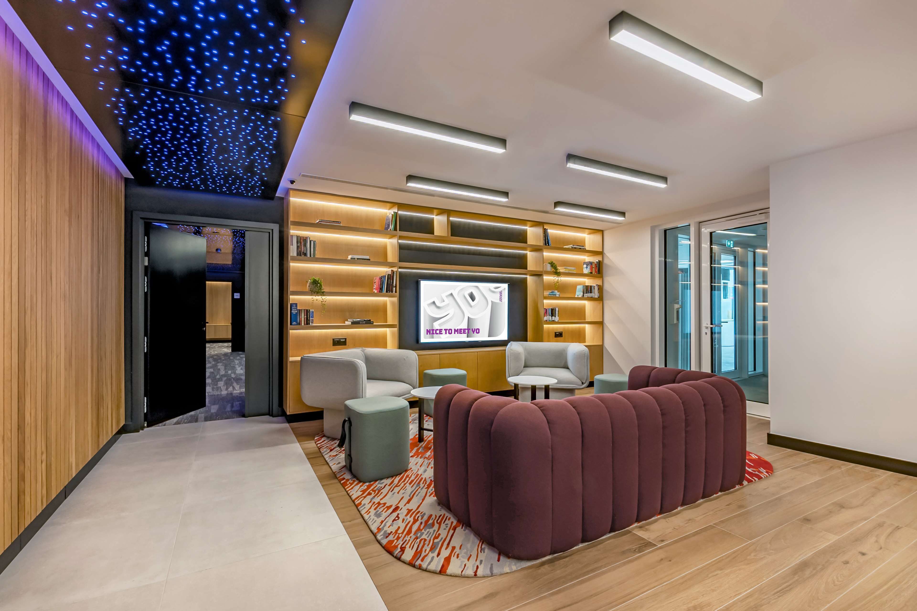 A modern lounge area with a flat-screen TV, comfortable seating, and a ceiling with blue lights.