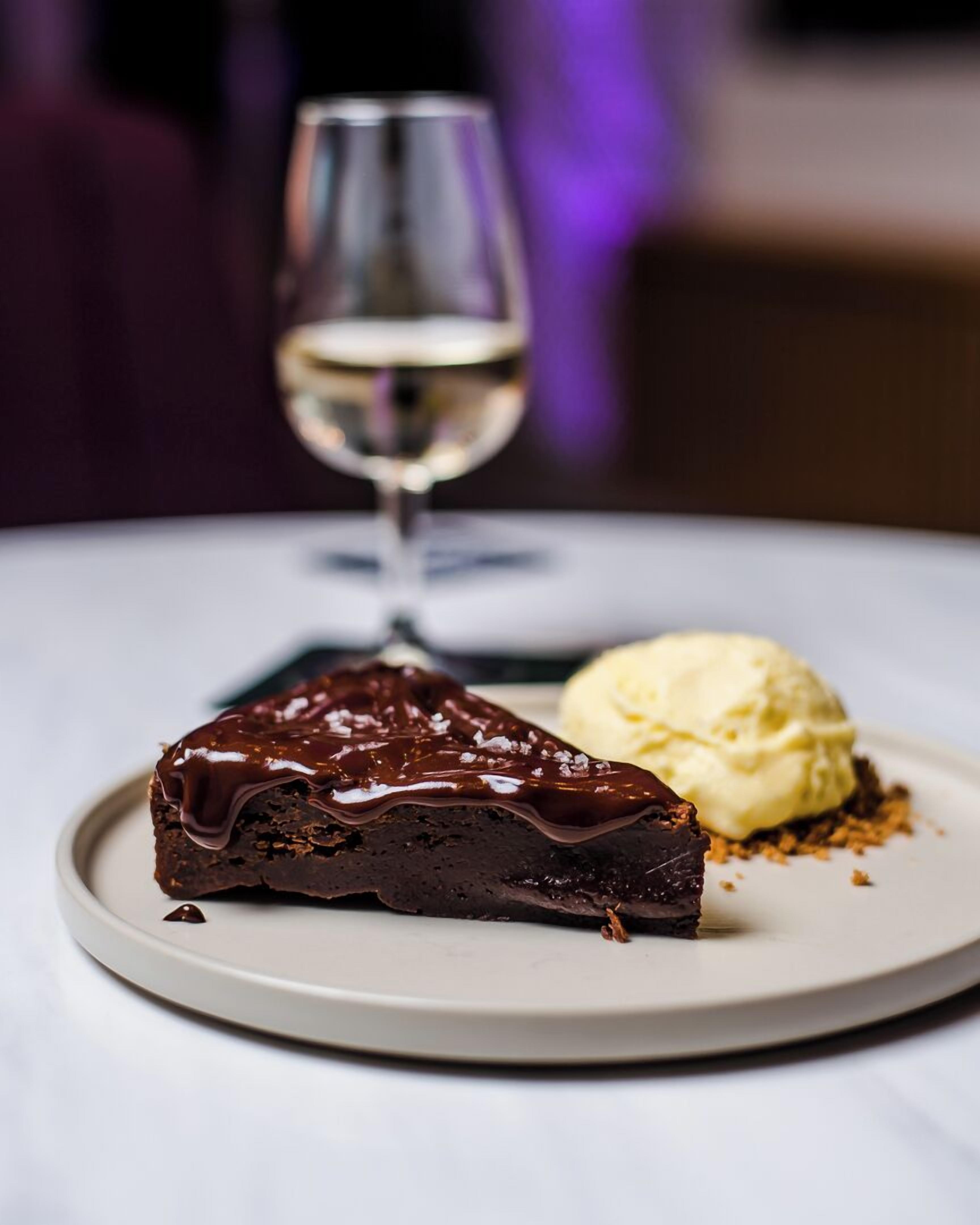 Una rebanada de pastel de chocolate con glaseado brillante y una bola de helado de vainilla sobre un plato blanco.