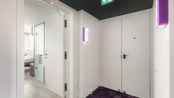 A hotel corridor with a purple geometric patterned floor, white doors, and a visible room with a bed and a towel hanging on the door.