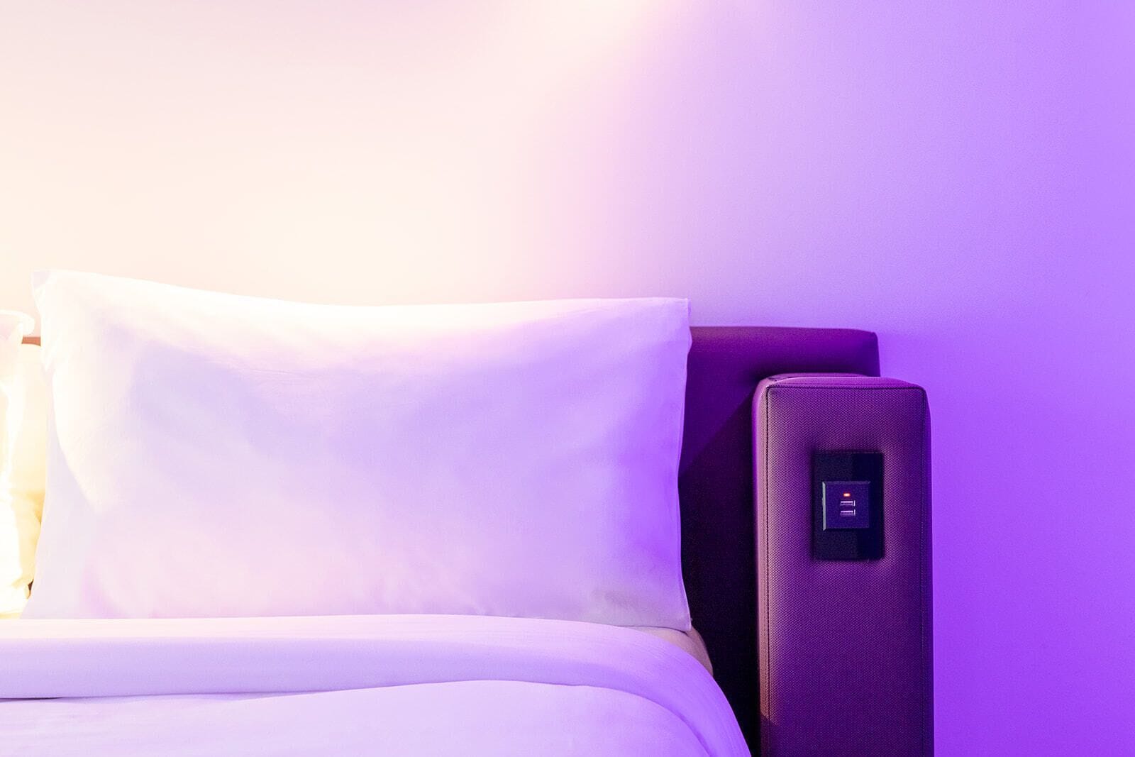 Una cama con un almohadón blanco y cabecera con panel de control.