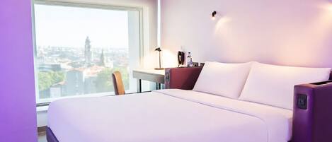 A hotel room with a large bed, a desk, and a view of a cityscape.