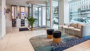 A modern hotel lobby with a reception desk, seating area, and a view of the street outside. - YOTEL Porto (Porto)