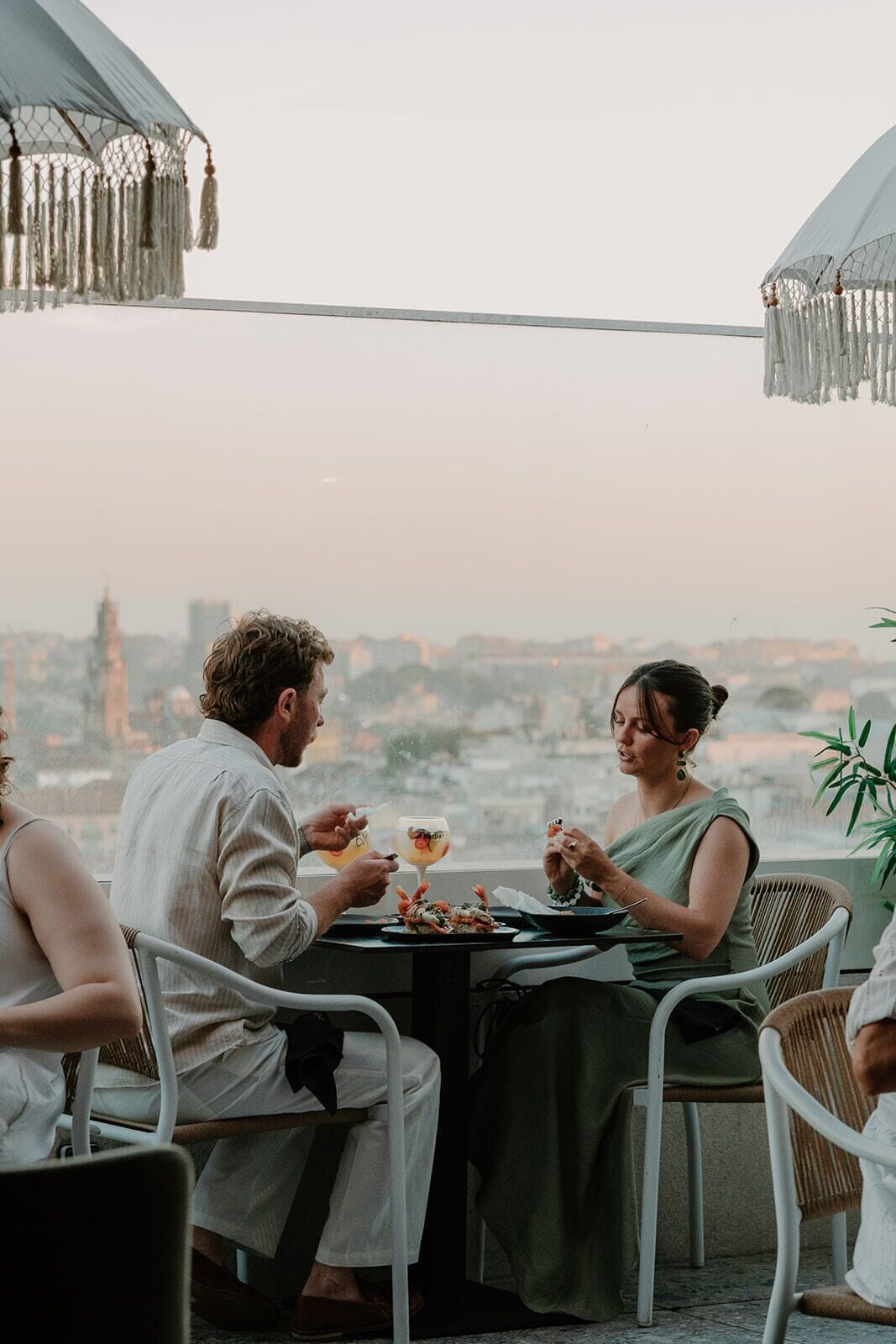 Una mesa de comedor con dos personas sentadas, un paisaje urbano al fondo y un cielo despejado.
