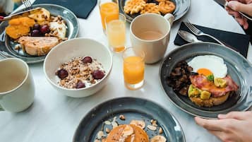 A breakfast setting with various dishes, including pancakes, eggs, and fruit, on a round table.