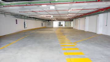 A clean, empty parking garage with yellow lines marking parking spaces and visible pipes and ducts on the ceiling.