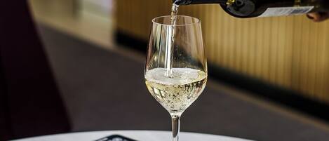 Une bouteille de vin blanc est versée dans un verre posé sur une table, à côté d’une assiette de nourriture.