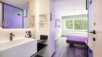 A modern hotel room with a bathroom, a bed, and a window with a view of greenery.