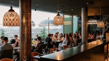 Un restaurante con una barra larga, lámparas colgantes con diseños y vistas a la ciudad.
