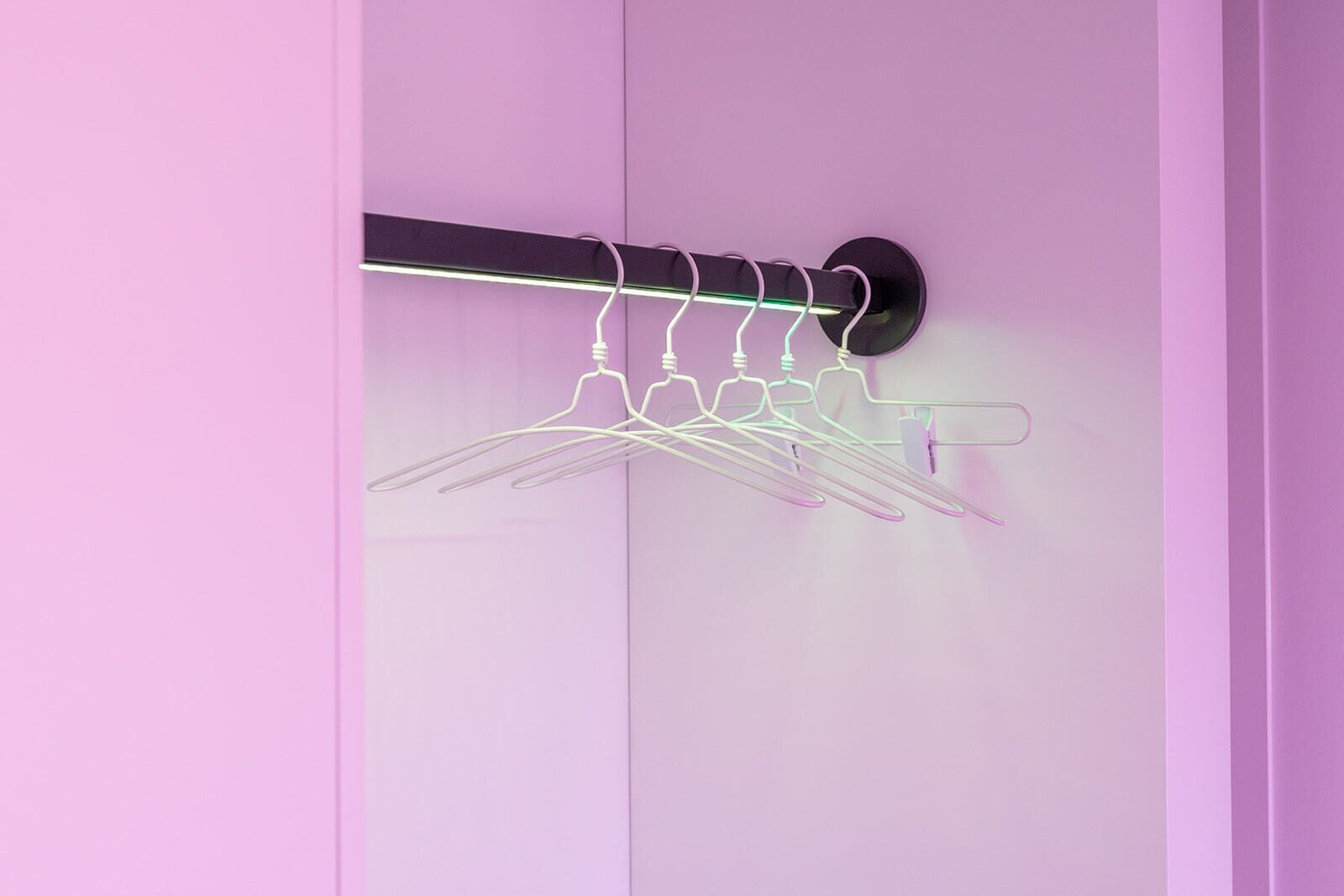 A wall-mounted coat rack with multiple hooks against a pink wall.