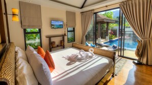 A hotel room with a large bed, a TV, a window with a view of a pool and greenery, and a ceiling fan. - Tulip Pool Villa (Rawai)