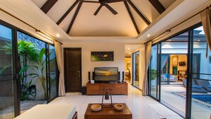 A spacious living room with a large TV, wooden coffee table, and a view of a swimming pool through large glass doors. - Tulip Pool Villa (Rawai)
