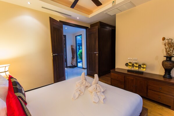 A hotel room with a neatly made bed, a wooden dresser, and a view of the outdoor area through an open door. - Tulip Pool Villa (Rawai)